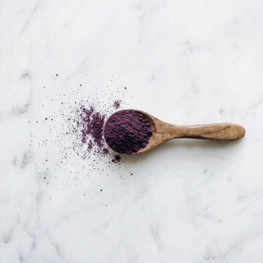 Cuchara de madera con ube en polvo morado sobre mármol blanco