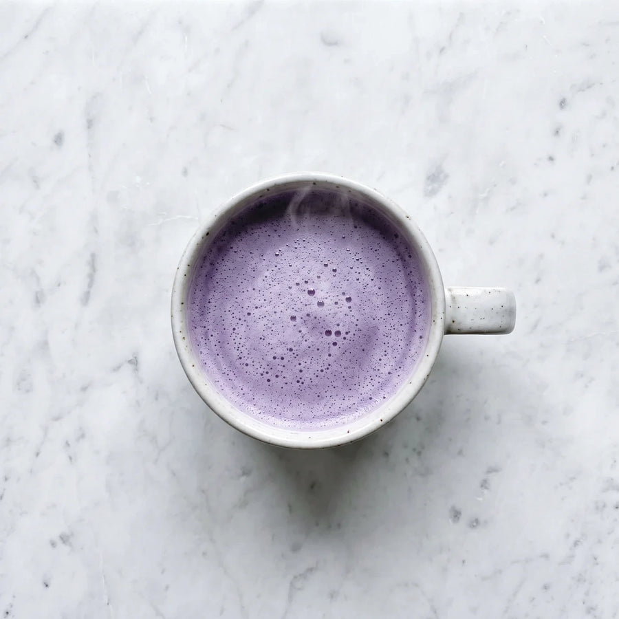 Taza de ube latte morado vista desde arriba sobre mármol blanco